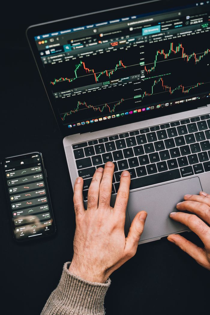 about-01 Hands typing on a laptop with cryptocurrency charts and smartphone display in view, focusing on digital finance.